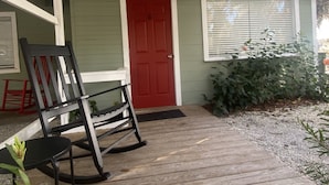 A wooden porch with a rocking chair, a red door, and a window with blinds. - Relax by the River - Shell Harbour Room 4 on the St Johns River (Satsuma)