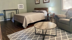 A bedroom with a bed, a round coffee table, a chair, a desk, and a ceiling fan. - Relax by the River - Shell Harbour Room 4 on the St Johns River (Satsuma)