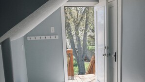 A room with a sloped ceiling, a bench, a small table, a door leading to an outdoor area with a wooden deck and trees.