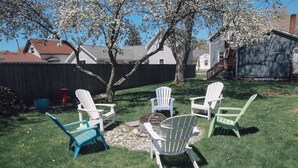 A backyard with four Adirondack chairs, a fire pit, and a wooden deck.
