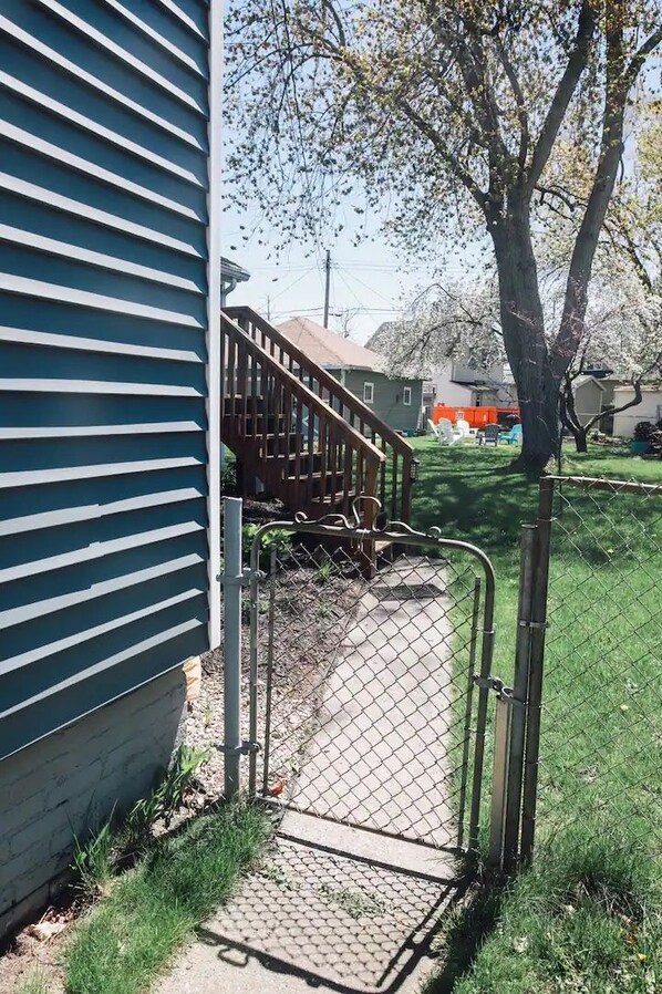A residential property with a fenced yard, a wooden staircase, and a metal gate leading to a concrete pathway.