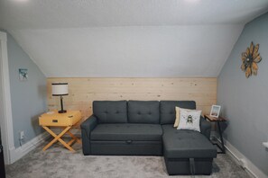 A cozy room with a grey sectional sofa, a wooden accent wall, and a small wooden side table with a lamp. - Great 1 Bedroom Downtown Grand Haven (Grand Haven)