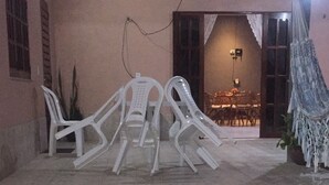 Une terrasse extérieure avec des carreaux à motifs hexagonaux, des chaises en plastique blanches et un hamac.