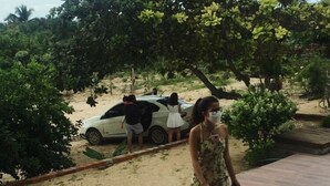 Une femme se tient sur une terrasse carrelée, avec une voiture blanche et des arbres en arrière-plan.