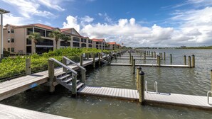 A waterfront hotel with a dock extending into the water, surrounded by lush greenery and a clear sky.