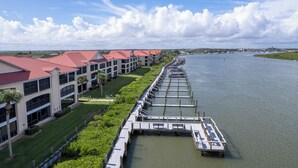 A waterfront hotel with a dock extending into the water, featuring multiple buildings with red roofs and a well-maintained lawn.