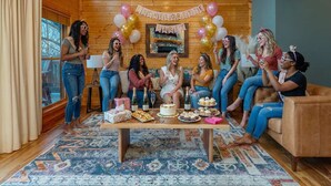 A cozy room with wooden walls and a fireplace, decorated for a party with balloons and a banner.