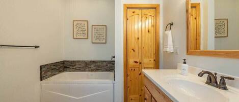 Un baño con bañera, lavabo, armarios de madera y una puerta.