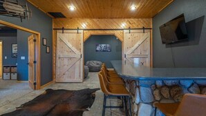 A rustic interior with a stone bar, wooden ceiling, and a large black rug.