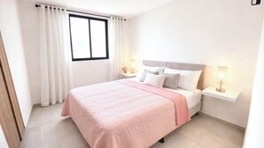 Een keurig opgemaakte slaapkamer met een bed, witte gordijnen, bedlampen en een raam.