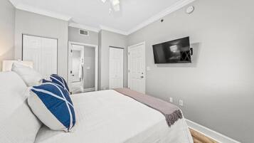 A bedroom with a bed, a ceiling fan, a TV, and a door leading to a bathroom.