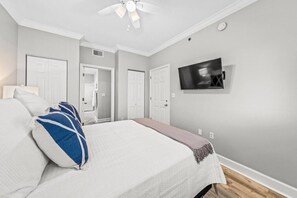 A bedroom with a bed, a ceiling fan, a TV, and a door leading to a bathroom.