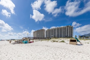 Un hotel frente a la playa con un edificio grande, un camino de madera y una caseta de salvavidas.