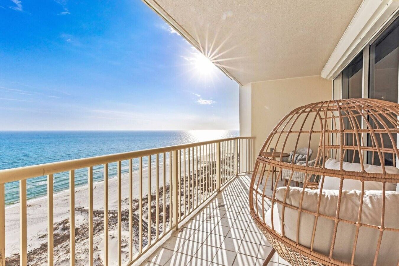A balcony with a view of the ocean, a wicker chair, and a railing.