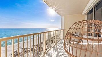 A balcony with a view of the ocean, a wicker chair, and a railing.