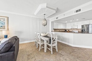 Une cuisine moderne avec des meubles blancs, un réfrigérateur en acier inoxydable et un coin repas comprenant une table et des chaises blanches.