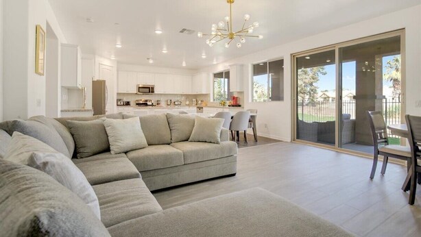 A spacious living area with a sectional sofa, a dining table with chairs, a kitchen with white cabinets, and a large sliding glass door leading to an outdoor patio. - NEW! Glamorous Golf Getaway w/ Private Pool & Spa (Indio)