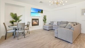 A living room with a fireplace, a gray sectional sofa, a dining table with chairs, and a ceiling light fixture. - NEW! Glamorous Golf Getaway w/ Private Pool & Spa (Indio)