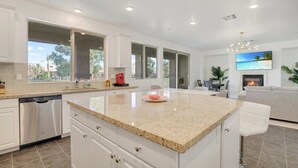A modern kitchen with a large island, white cabinetry, and a view of the outdoors. - NEW! Glamorous Golf Getaway w/ Private Pool & Spa (Indio)