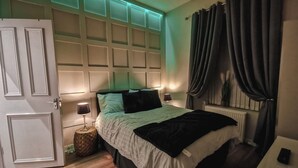 Ein Schlafzimmer mit Bett, Nachttischlampen, einem Nachttisch, einer Tür und einem Fenster mit Vorhängen.