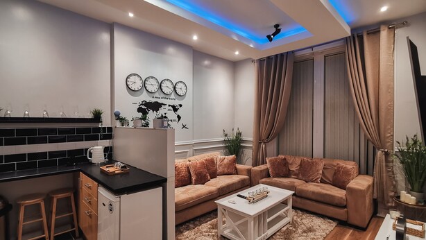 Ein modernes Wohnzimmer mit Sofa, Couchtisch und Küchenzeile mit Theke und Hockern.