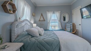 Une chambre à coucher avec un lit, une chaise, une télévision et une fenêtre avec des rideaux.