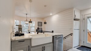 A modern kitchen with a large island, stainless steel appliances, pendant lighting, and a view to the outside.