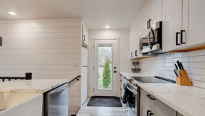 A modern kitchen with white cabinetry, stainless steel appliances, and a view through the door.