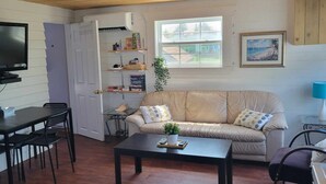 A cozy living room with a TV, a sofa, a coffee table, and a dining area. - Beach vibes (Pointe-du-Chêne)