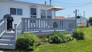 A two-story house with a white exterior, a front porch with a railing, and a sign indicating it's a cottage rental. - Beach vibes (Pointe-du-Chêne)