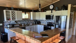Une cuisine moderne avec des meubles blancs, un îlot central doté de tabourets, un four à micro-ondes, une cuisinière et un évier.