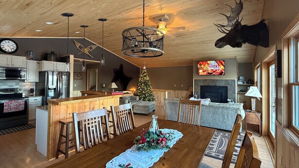 Un vaste espace de vie doté d’un plafond en bois, d’une table à manger avec des chaises, d’un sapin de Noël et d’une tête d’élan fixée au mur.