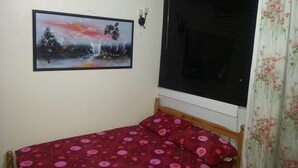Une petite pièce avec un lit simple, une fenêtre avec des stores, un tableau accroché au mur et un rideau à motifs floraux.
