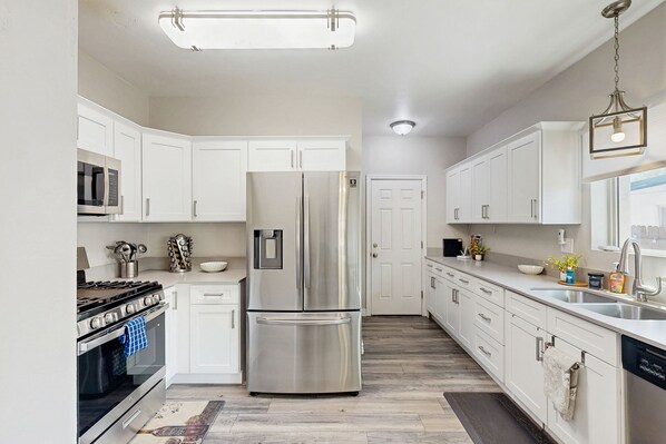 Kitchen features a central island with a sink and a hanging light fixture, stainless steel appliances, and a double-door refrigerator.