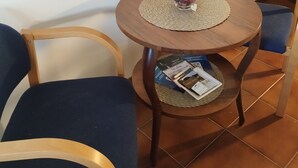 Ein kleiner, runder Holztisch mit einer gewebten Tischmatte, zwei blau gepolsterten Stühlen und einer Glasvase mit Blumen.