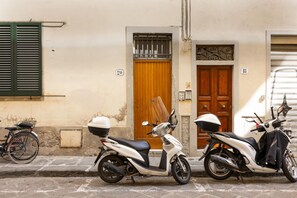 Deux scooters garés sur une rue pavée, un vélo et un immeuble dont les portes sont numérotées.
