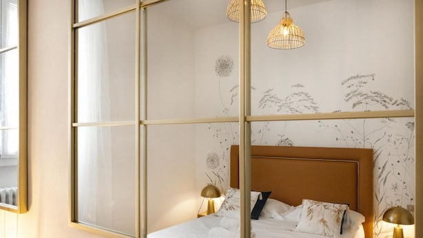 Ein Schlafzimmer mit großem Fenster, einem Bett mit weißer Bettwäsche, zwei Nachttischlampen und einer Wand mit Blumenmuster-Tapete.