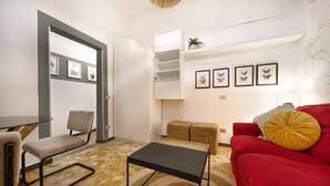 Ein Wohnzimmer mit einem roten Sofa, einem kleinen Tisch, einem Sessel und einem weißen Schrank mit Regalen.