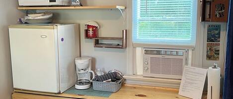 Une cuisine compacte équipée d’un réfrigérateur, d’un four à micro-ondes, d’une machine à café et d’une fenêtre avec des stores.