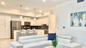 A modern living room with a white sectional sofa, a glass coffee table, and a blue rug. - Cozy 2BD/2BA Condo Near Disney 270 (Kissimmee)