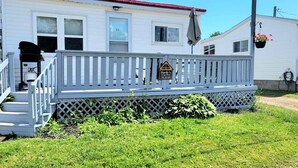 A mobile home with a white exterior, a porch with a railing, and a small garden area. - Home by the beach (Pointe-du-Chene)