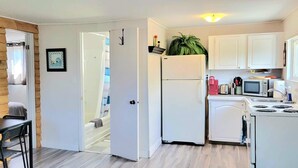 A compact kitchen with white cabinets, a refrigerator, a microwave, and a sink. - Home by the beach (Pointe-du-Chene)