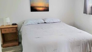 A bedroom with a bed, a nightstand, a lamp, and a painting on the wall. - Home by the beach (Pointe-du-Chene)