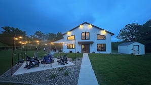 Une maison moderne à deux étages, dotée d’un patio couvert, d’un espace salon extérieur et d’un petit abri de jardin.