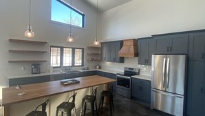 Une cuisine moderne dotée d’un îlot central, d’appareils électroménagers en acier inoxydable et de luminaires suspendus.