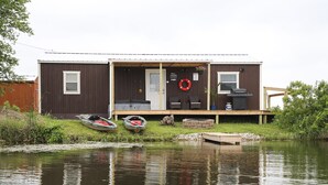 Eine kleine Holzhütte mit Steg, Kajaks und Grill.
