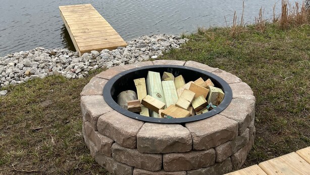 Ein Deck am Seeufer mit einem Feuerkorb aus Stein und einem hölzernen Steg, der sich ins Wasser erstreckt.