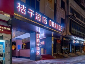 A hotel entrance with a prominent neon sign, a staircase leading to the entrance, and a visible side entrance. - Orange Hotel Donghui Citymall Zengcheng Guangzhou (Guangzhou)