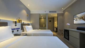 A hotel room with two beds, a desk, a mirror, and a shower area.