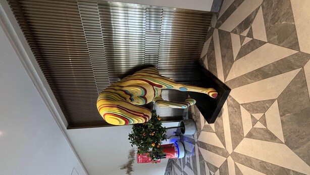 A lobby with a patterned floor, a large decorative sculpture, and a potted plant.